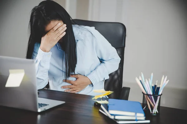 Young asian business woman person sitting at work and has stress pain in her stomach. Concept office syndrome abdomen pain from occupational disease, Female having belly pain and using laptop computer