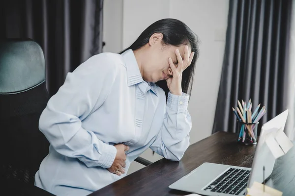 Young asian business woman person sitting at work and has stress pain in her stomach. Concept office syndrome abdomen pain from occupational disease, Female having belly pain and using laptop computer