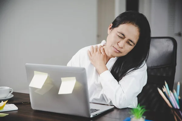 Young asian woman is sitting at work and has tension pain in her neck. Concept office syndrome backache pain from occupational disease, Female having muscle pain from using laptop computer, back pain.