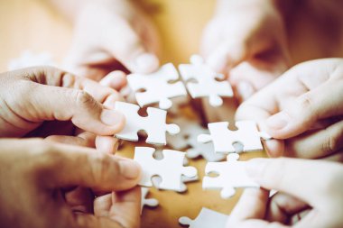 Hands of a person little child and parent playing jigsaw puzzle piece game together on wooden table at home, concept for leisure with family, play with children's development, education and fun.