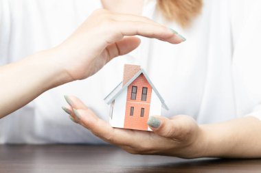 Hands of a woman surround a house model. real estate, insurance and property concepts