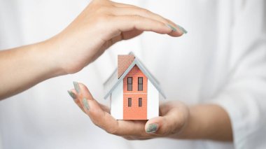 Hands of a woman surround a house model. real estate, insurance and property concepts