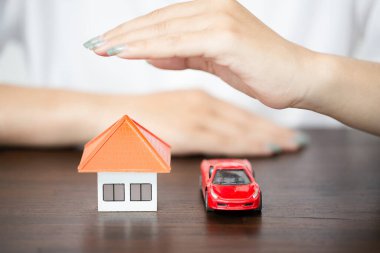 young woman use left hand to protect house model and toy car. real estate, insurance and property concepts