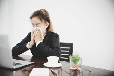 Sick young asian business woman sitting alone at work sneeze holding tissue handkerchief and blowing wiping her running nose. 
