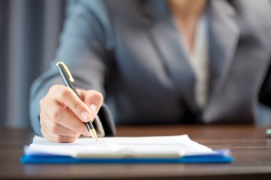 Workplace closeup person professional businesswoman sitting at desk hold pen signing or signature contract paper. Employee woman writing agreement document on paperwork form corporate at work office