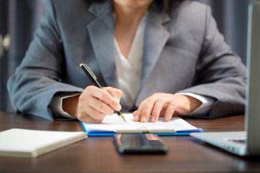 Workplace closeup person professional businesswoman sitting at desk hold pen signing or signature contract paper. Employee woman writing agreement document on paperwork form corporate at work office