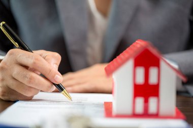 Woman home sales person is checking documents for house purchase contract before letting the customer sign contract on table is key with house model, real estate trading and insurance property concept