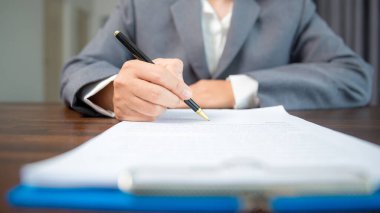 Workplace closeup person professional businesswoman sitting at desk hold pen signing or signature contract paper. Employee woman writing agreement document on paperwork form corporate at work office