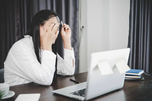 Young business woman person sleepy and has frustration eye problems with cephalalgia disease from using laptop computer on her office desk. Stressed female employee tired and exhausted from overwork.