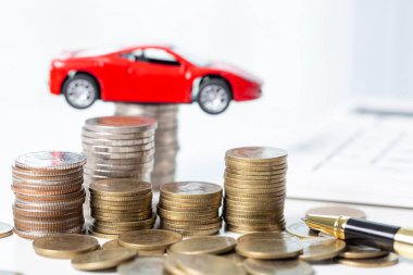 Arka planda bozuk para yığını olan oyuncak araba. Ulaşım finansmanını yönetmeyi planlıyorum. Araba sigortası işi kavramı, tasarruf satın alma - yeni araba için vergi ve kredi ile satış.