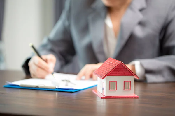 Woman home sales person is checking documents for house purchase contract before letting the customer sign contract on table is key with house model, real estate trading and insurance property concept