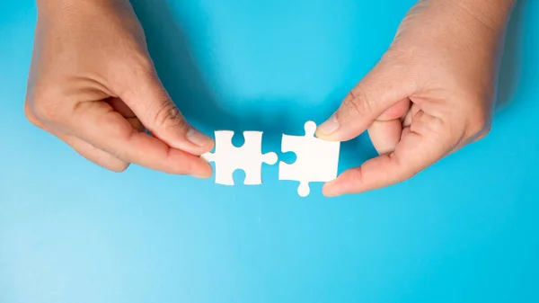 Close up hand holding and playing jigsaw game incomplete. White part of jigsaw puzzle pieces on blue background. concepts of problem solving, business, teamwork.