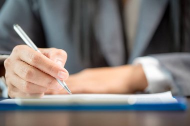 Workplace closeup person professional businesswoman sitting at desk hold pen signing or signature contract paper. Employee woman writing agreement document on paperwork form corporate at work office