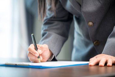 Workplace closeup person professional businesswoman sitting at desk hold pen signing or signature contract paper. Employee woman writing agreement document on paperwork form corporate at work office