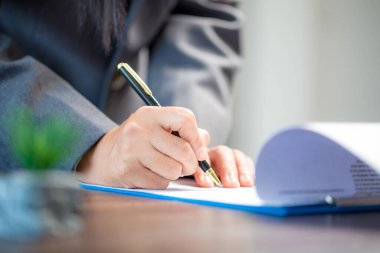 Workplace closeup person professional businesswoman sitting at desk hold pen signing or signature contract paper. Employee woman writing agreement document on paperwork form corporate at work office