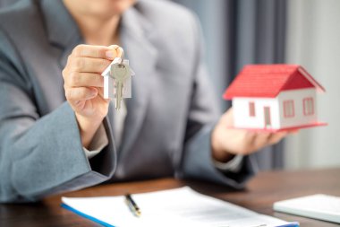 Woman home sales person is checking documents for house purchase contract before letting the customer sign contract on table is key with house model, real estate trading and insurance property concept