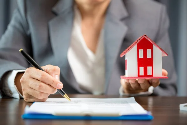 Woman home sales person is checking documents for house purchase contract before letting the customer sign contract on table is key with house model, real estate trading and insurance property concept