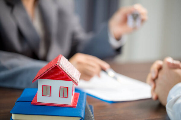 Woman home sales person is checking documents for house purchase contract before letting the customer sign contract on table is key with house model, real estate trading and insurance property concept
