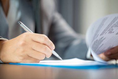 Workplace closeup person professional businesswoman sitting at desk hold pen signing or signature contract paper. Employee woman writing agreement document on paperwork form corporate at work office