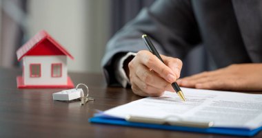 Woman home sales person is checking documents for house purchase contract before letting the customer sign contract on table is key with house model, real estate trading and insurance property concept