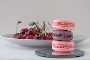 Close-up of appetizing mix of macarons on light background. Blurred plate with red cherries in background. Selective focus. Excellent image for dessert banners and advertisements. Place for your text.
