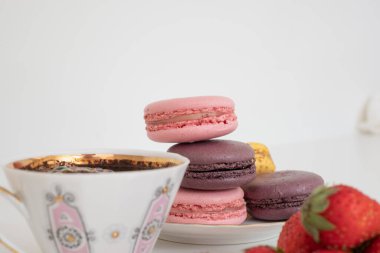 Mix of appetizing macarons on plate on white background with black coffee in porcelain cup and strawberries in the foreground. Excellent image for dessert banners and advertisements. Place for your text.