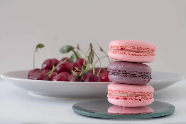 Close-up of appetizing mix of macarons on light background. Blurred plate with red cherries in background. Selective focus. Excellent image for dessert banners and advertisements. Place for your text.