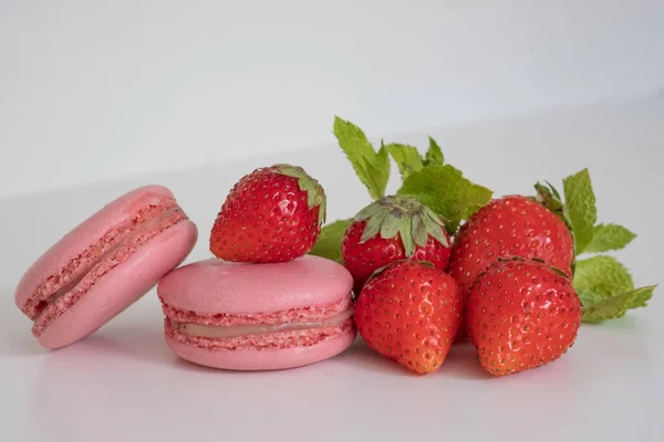 Appetizing pink macarons and fresh strawberries on white background. Excellent image for dessert banners and advertisements. Place for your text.