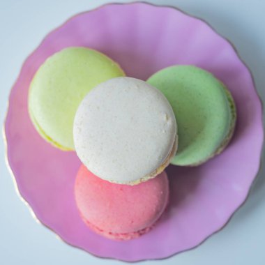 Top view of colorful macarons in pink plate. Light blue background. Sweet concept. Flat lay. Excellent image for dessert banners and advertisements. Place for your text.