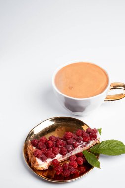 Delicious piece of cake with fresh raspberries and luxurious cup of coffee in background. Light grey background. Sweet concept. Excellent image for dessert banners. Place for your text.
