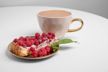Delicious piece of cake with fresh raspberries and luxurious cup of coffee in background. White table. Light grey background. Sweet concept. Excellent image for dessert banners. Place for your text.