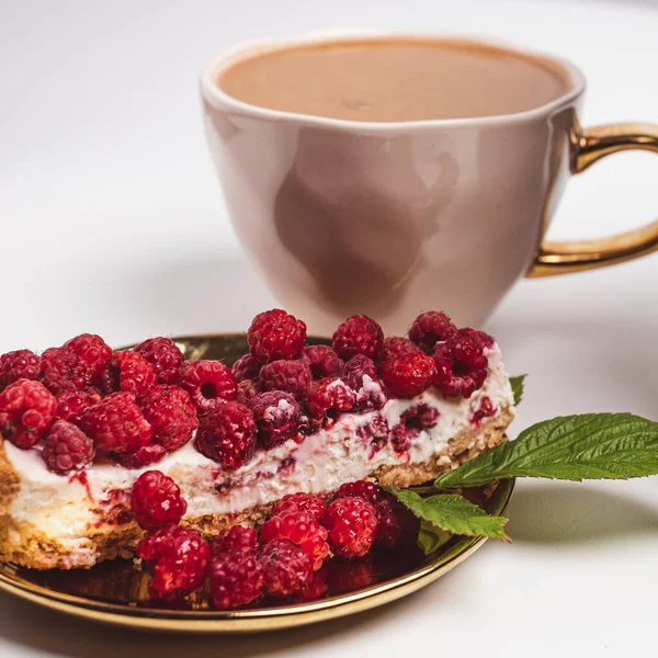 Close-up of delicious piece of cake with fresh raspberries on golden plate. Luxurious cup of coffee in background. White background. Sweet concept. Excellent image for dessert banners. Place for your text.