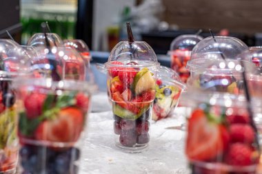 Delicious, colorful and fresh fruit pieces salad in plastic glasses placed on table. Blurred background.