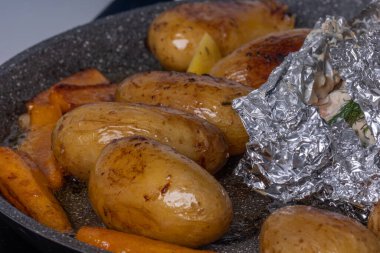 Close-up of appetizing oven baked potatoes, carrots and baked salmon in foil. Served on gray plate. Excellent image for homemade food banners and advertisements.