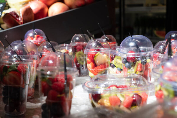 Вкусные, красочные, свежие ягоды и фруктовые кусочки салата в пластиковых стаканах помещены на ледяной стол. Размытый фон.