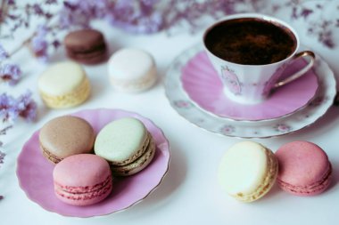 İştah açıcı badem kurabiyeleriyle porselen bardaktaki lezzetli kahvenin karışımı. Beyaz masa üzerinde bulanık çiçeklerle süslenmiş. Kuru çiçekler. Tebrik kartı.