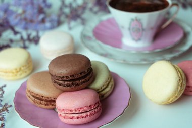 İştah açıcı badem kurabiyeleriyle porselen bardaktaki lezzetli kahvenin karışımı. Beyaz masa üzerinde bulanık çiçeklerle süslenmiş. Kuru çiçekler. Tebrik kartı.