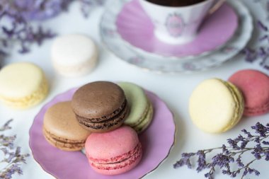 İştah açıcı badem kurabiyeleriyle porselen bardaktaki lezzetli kahvenin karışımı. Beyaz masa üzerinde bulanık çiçeklerle süslenmiş. Kuru çiçekler. Tebrik kartı.