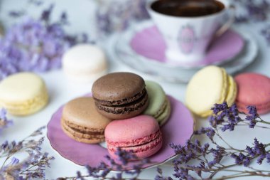 İştah açıcı badem kurabiyeleriyle porselen bardaktaki lezzetli kahvenin karışımı. Beyaz masa üzerinde bulanık çiçeklerle süslenmiş. Kuru çiçekler. Tebrik kartı.