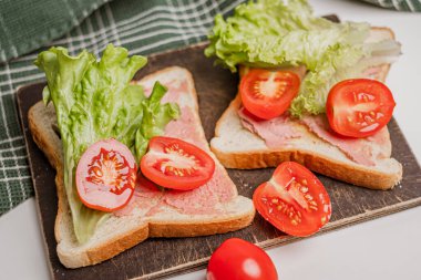 Mikroyeşillikler, domatesler ve taze marullarla süslenmiş lezzetli tostların yakın çekimi. Sağlıklı kahvaltı. Arka planda yeşil havlu var. Beyaz arkaplan.