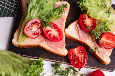 Mikroyeşillikler, domatesler ve taze marullarla süslenmiş lezzetli tostların yakın çekimi. Sağlıklı kahvaltı. Arka planda yeşil havlu var. Beyaz arkaplan.
