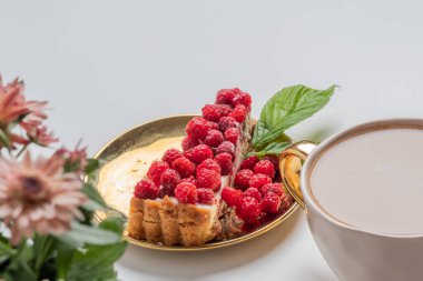 Goden tabağında taze ahududu olan lezzetli bir parça kek, altın devedikeni olan bir fincan kahve. Güzel kavram. Tatlı afişleri ve reklamları için mükemmel bir imaj. Göz kamaştırıcı bir yaşam tarzı, hedonik tatiller, güzel bir dinlenme, sevgi dolu bir eğlence, hayattan zevk alma.