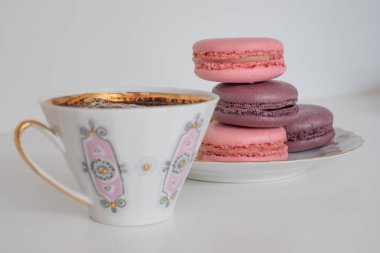 İştah açıcı pembe, mor badem kurabiyesi ve beyaz arka planda bir fincan kahve. Beyaz masada iştah açıcı badem ve lezzetli kirazların karışımı. Tebrik kartı. Tatlı konsepti. Tatlı afişleri ve reklamlar için mükemmel bir imaj. Metin için yer.