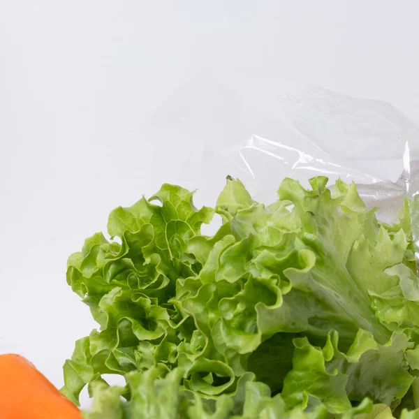 Close-up of fresh salad in plastic bag with fresh carrot in the foreground.