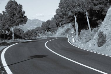 Resimli kırmızı kil kayalıklar boyunca boş dolambaçlı yol kısmen ağaçlarla ve mavi gökyüzü ve arka planda beyaz bulutlarla kaplı çalılarla kaplı. Güneşli bir yaz günü.