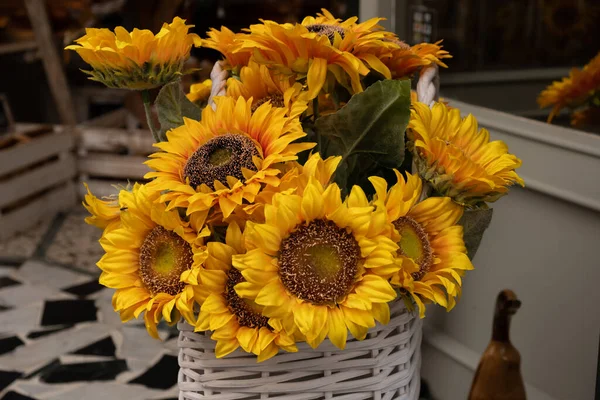 Close-up of fresh yellow sunflower bouquet in the white wicker basket placed on white windowsill with sunflower bouquet mirror image in background