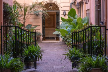 Yenilenmiş kadim kapıları olan etkileyici avlu manzarası. Avludaki açık yeşil bitkiler. Ön planda siyah vintage metal kapı açıldı..