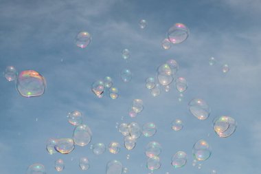 Mavi berrak gökyüzü manzarası ve arka planda bulutlar ve güneşli bir yaz gününde ön planda uçan sabun köpükleri, çocuklar için zevk, parti havası, ekolojik olmayan