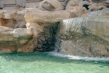 Dünyanın en ünlü simgelerinden biri olan Trevi Çeşmesi Roma 'nın parlak güneş ışığında ön planda su havzası ile çevrilidir..