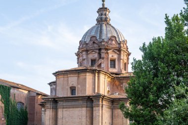 Arka planda mavi gökyüzü ve ön planda antik metal çitlerle kilisenin etkileyici manzarası. Santi Luca ve Martina. Roma.